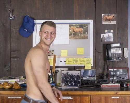Shirtless young white man in front of an office wall with phone and photographs