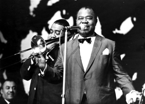 Louis Armstrong at the microphone with a trombone player behind him