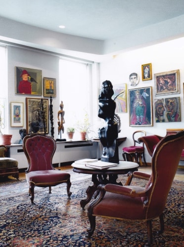 The Gross living room, featuring a table, chairs, and a large rug. On the table and the walls are works found within the Chaim Gross art collection.