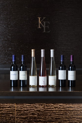 Kenzo Estate wines in half-bottle lineup left to right: asuka, rindo, asatsuyu, yui, muku, ai, murasaki wth KE logo behind
