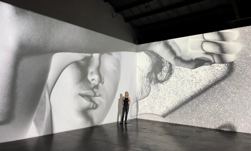 Artist Mona Kuhn stands inside her multi-wall installation where her photographs are projected onto gallery walls.