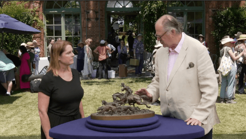 Eric Silver and a guest at Antiques Roadshow, with a table in front of them with a bronze sculpture of a horse and rider with hunting dogs
