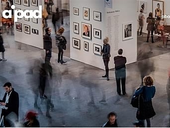 Time lapse photo of people walking through the halls of The Photography Show and looking at framed installed photographs.