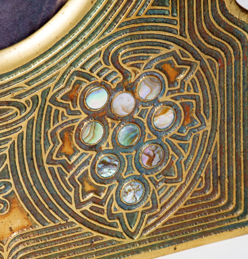 Detail of the lower edge of a Tiffany Studios Abalone Pattern Picture frame, showing inset circular discs of iridescent abalone shell which represent a grape cluster, surrounded by swirling vine-like lines of inset green enamel 