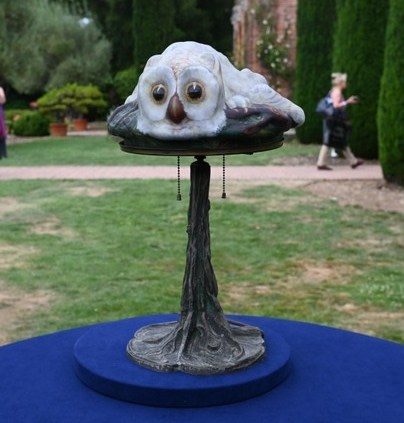 a table lamp with glass shade in the form of a crouching snowy owl with amber eyes, on a bronze base in the form of a tree trunk