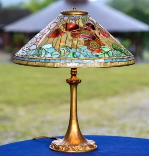 an antique tiffany lamp with cone shaped leaded glass shade depicting red poppies against gold background glass, with green leaves, on a gilt bronze base