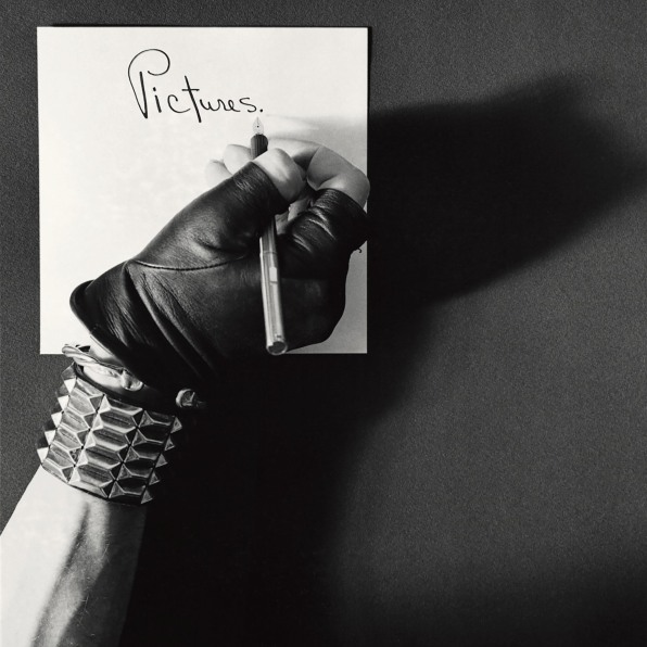 Robert Mapplethorpe's hand in leather glove and spiked bracelet writing the word "Pictures"