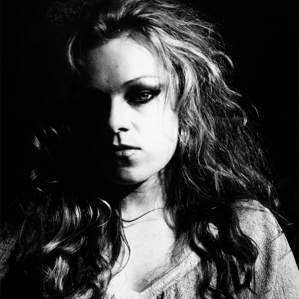 High contrast portrait of Cookie Mueller, with half her face in shadow.