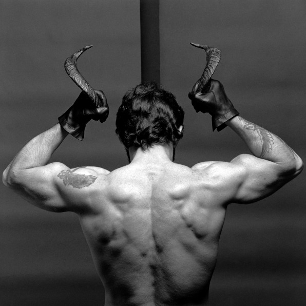 Nude white man facing away from camera from the torso up, holding horns.
