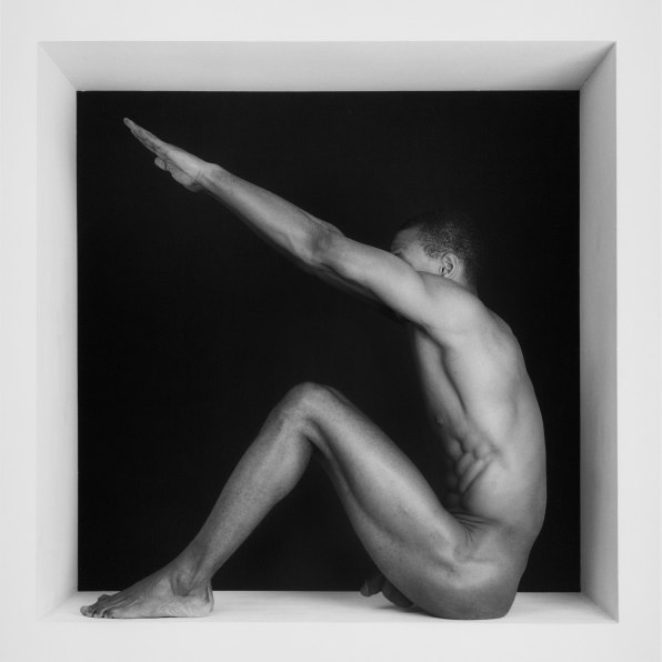 Thomas naked, sitting in a square with arms reaching up..