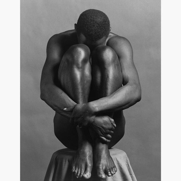 Ajitto posed on a stool with his head down holding his legs to his chest.