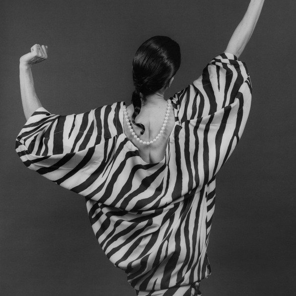 Lisa Lyon in zebra- patterned dress and pearls with hands up, facing away from camera