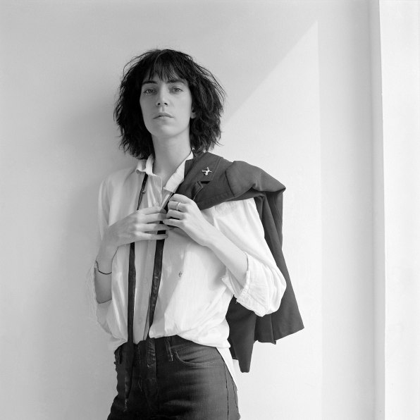 Patti Smith facing camera, suit jacket draped over shoulder, triangular patch of light behind her.