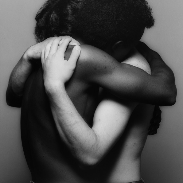 Two men, one white, one Black, embracing with faces obscured.
