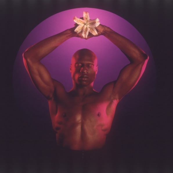 Portrait of Ken Moody holding up flower against a purple geometric background.
