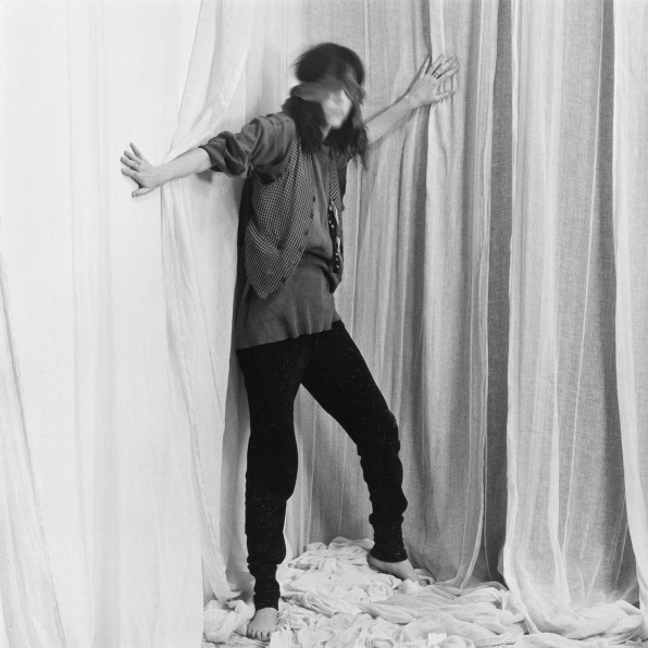 Blindfolded woman standing in front of cloth backdrop.