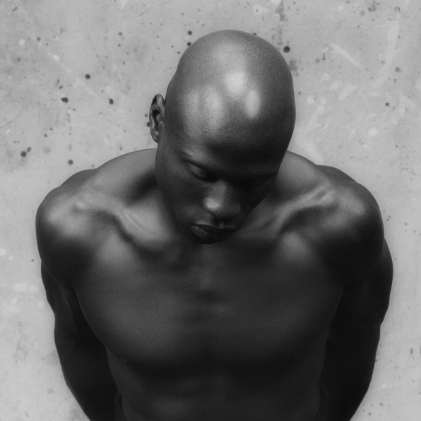 Ken Moody, nude from the chest up, looking downwards.