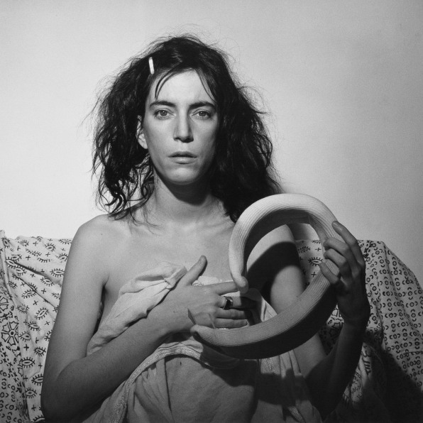 Patti Smith facing camera, wrapped in a sheet and holding neck brace.