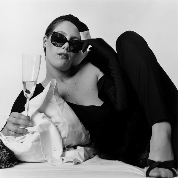 Portrait of white woman on bed holding champagne. 