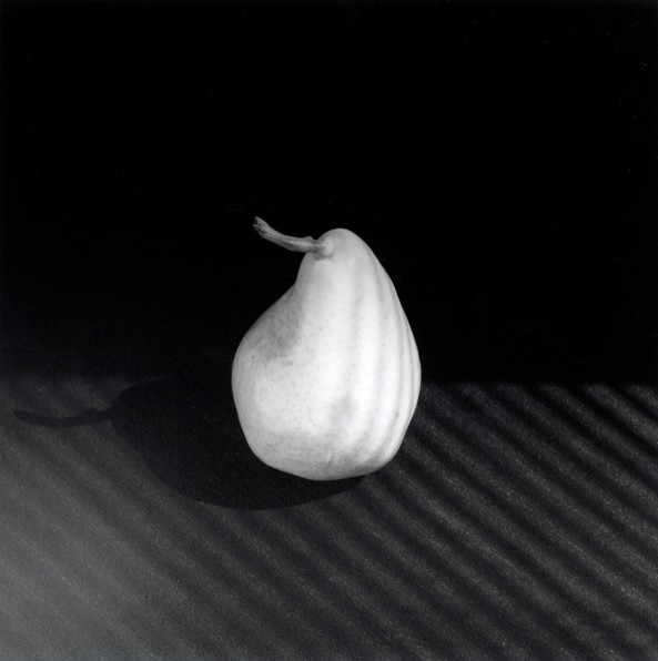 Pear atop shadowed table with dark background.