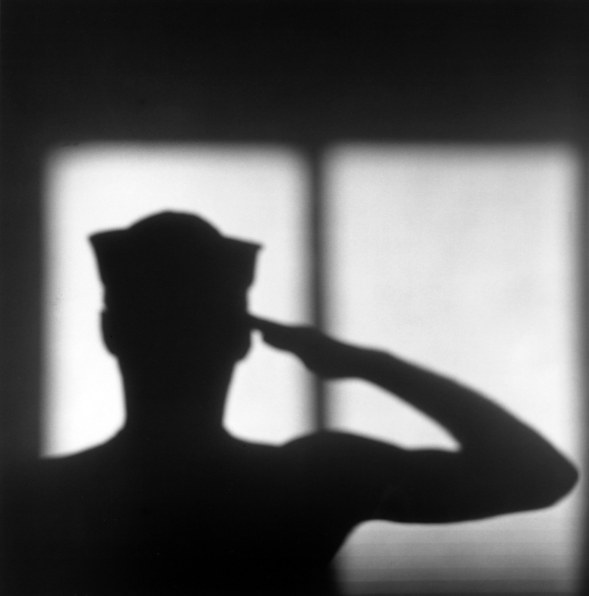 The shadow silhouette of a man in a Navy cap saluting.
