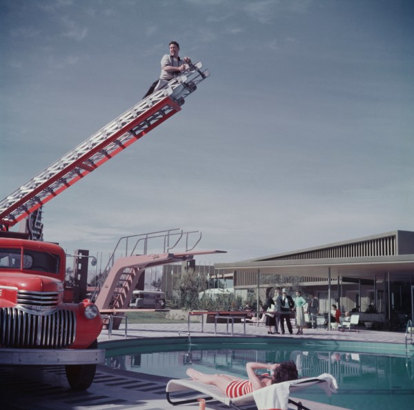 Slim Aarons, To Any Lengths, 1954: Slim Aarons photographing Mara Lane from the top of an extending ladder by the swimming pool at Sands Hotel, Las Vegas