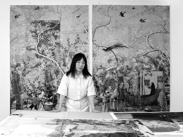 portrait of Kyungmi Shin in her studio standing behind a table with work laid out on it and with a large diptych hung on the wall behind her