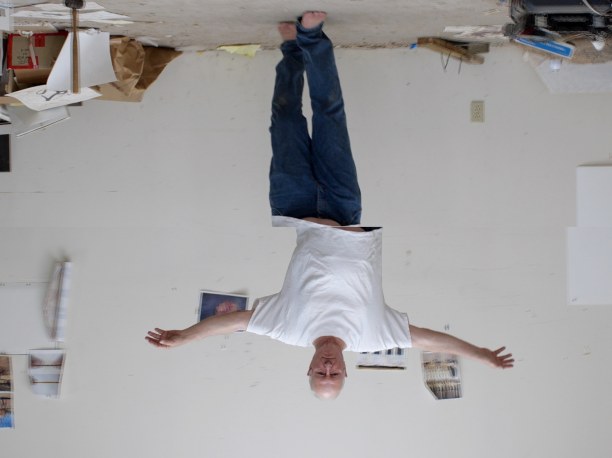 upside down image of a man in a tee shirt and jeans walking with his arms outstretched to the side