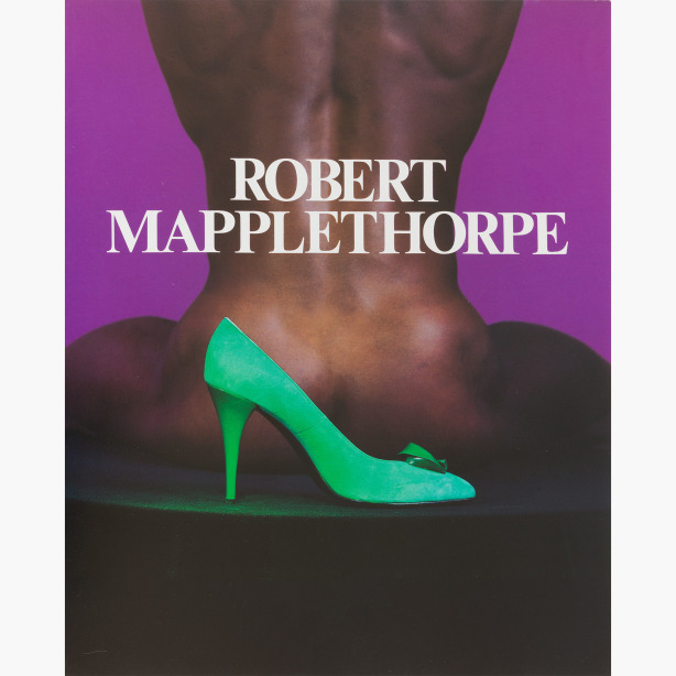 Color image of a bright green high-heeled shoe in front of a naked black man, seated and facing away from camera, against a purple background.