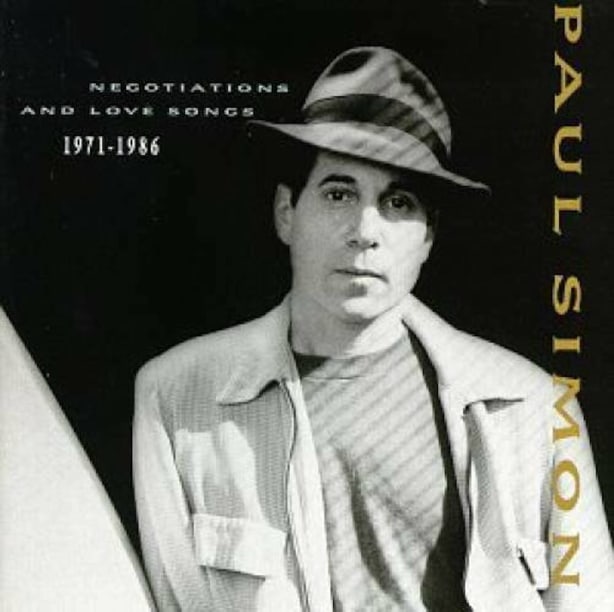 Album cover for Paul Simon's Negotiations and Love Songs 1971-1986, portrait of Paul Simon wearing a hat, looking at camera, with shadows on face and body.