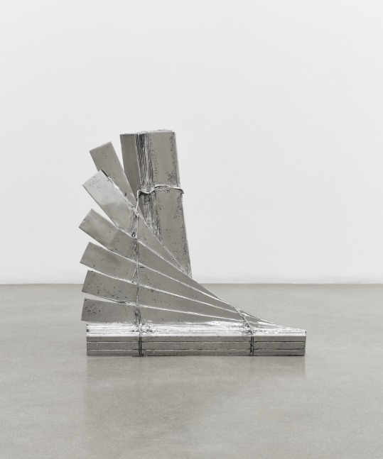 An aluminum sculpture of contorted window blinds on the floor.