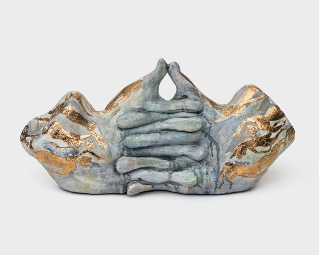 A blue ceramic sculpture of interlocked hands and golden painted figures.