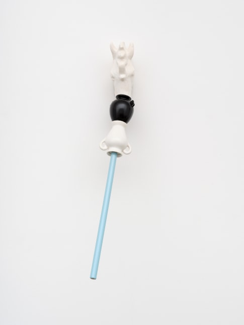 A composite ceramic sculpture with a wall mounted white head of a horse with its nose in a black jar connecting to a white vessel and blue pole extending out from the wall.