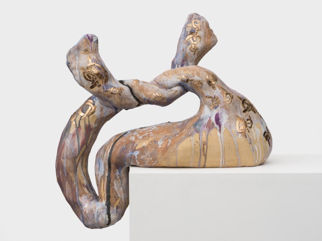 A ceramic sculpture that is knotted at the top and resting off the edge of the pedestal in streaking blue, brown and purple glazes.