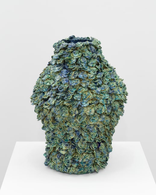 A blue and green ceramic vessel covered in layers of rose like floral shapes.