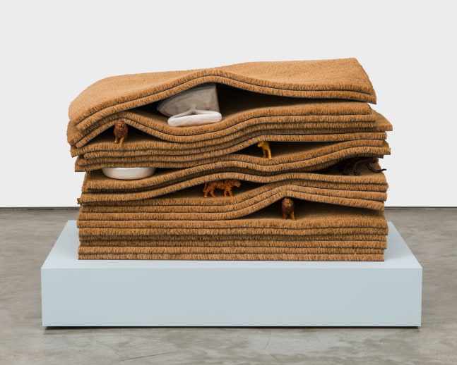 A sculpture with 20 layered doormats with ceramic animal figurines and ceramic irons peaking out from between the layers.