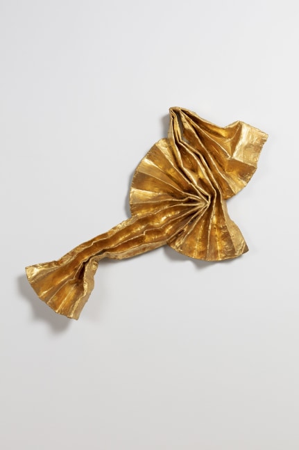 Pleated gold sculpture against a white wall