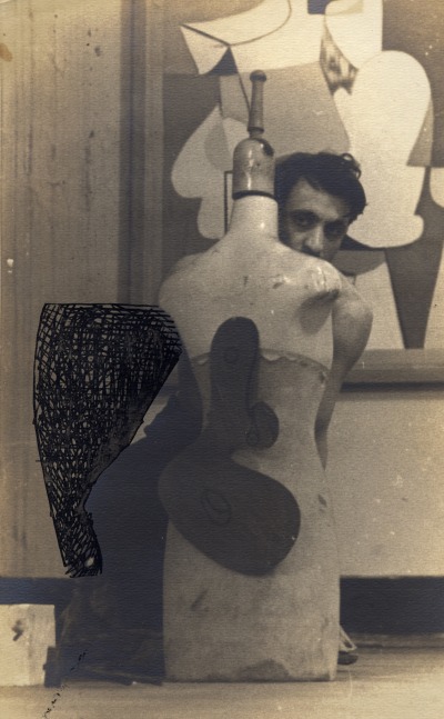 Young man in a studio hiding behind a mannequin with an abstract shape and behind him a detail of an abstract painting hanging on the wall