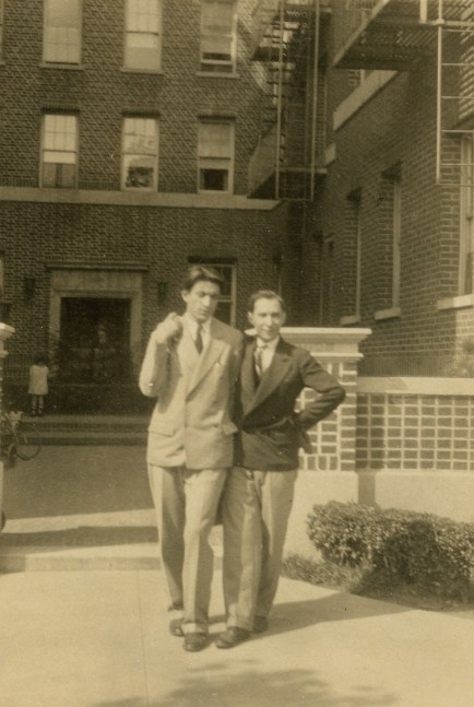 Sepia photograph of two males dressed in suits standing in the courtyard a large brick apartment building