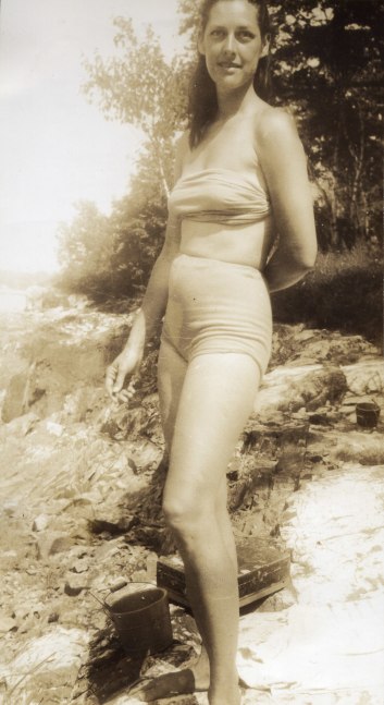Standing woman in a two-piece bathing suit posing on a rocky beach with one arm behind her back