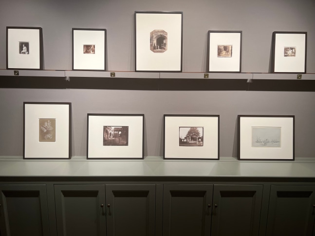 Installation photograph of 9 framed works in the exhibition in two rows, one above the other in the processional space