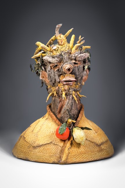Ceramic bust whose features are made of tree bark, with leaves for hair and a lemon and orange hanging from a branch protruding at the neck