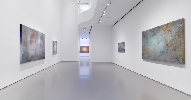 View of main gallery space with two large artworks hanging on opposite walls and farther artwork in the center