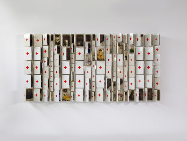 a large ceramic sculpture composed of first aid boxes of varying sizes filled with ceramic objects including a Buddha, honeycomb and pill bottles