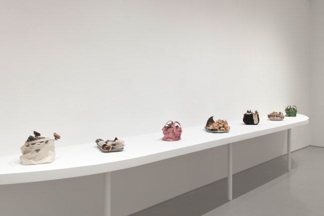 a white shelf holds seven sculptures resembling designer handbags and food trays