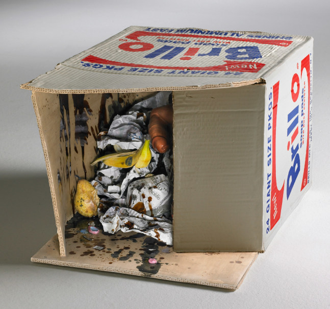 ceramic brillo box on its site and open to reveal fruit, balled up newspapers and a dildo