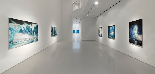 View of gallery featuring paintings of icebergs in varying shades of blue, white, and black
