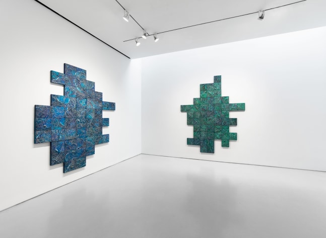 Blue and green geometric artworks hang on a white wall in a gallery space.