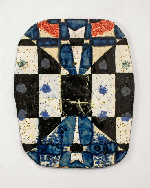 Oval ceramic wall piece with a patchwork of black, cream, red, and deep cobalt-blue glazed sections arranged in a quilt-like grid. The surface features speckled and bubbled textures, with areas of mottled blue resembling ink blots or water stains.