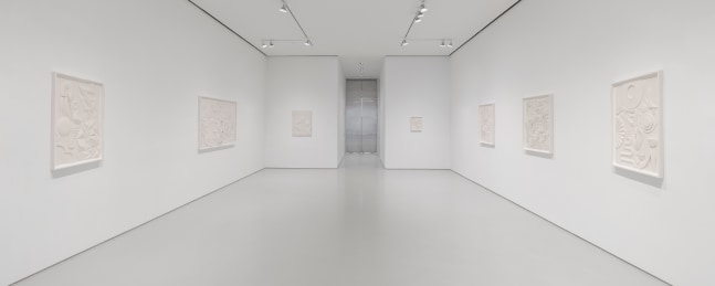 Installation view of white artworks on a white wall